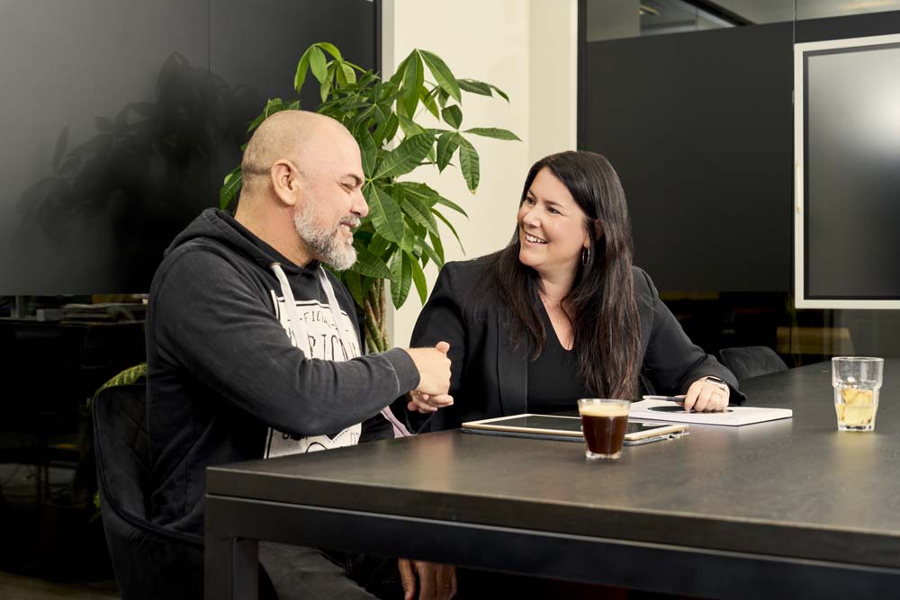 Man en vrouw schudden tevreden handen met een getekend contract op tafel